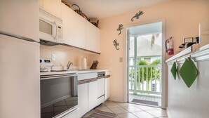 A kitchen with white cabinets, a microwave, an oven, and a dishwasher. There is a door leading to a balcony with a view of greenery. - Shipyard in Key West, FL (Key West)