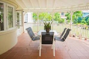 A covered patio with a table and two chairs, a potted plant, and a view of greenery. - Across The Bay 3 (Gros Islet)