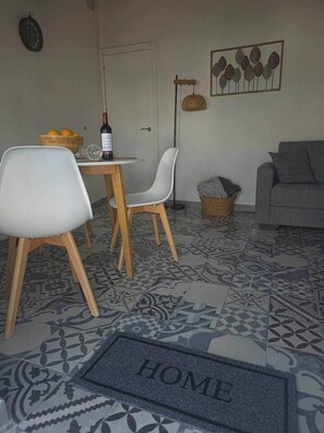 Een woonkamer met een bank, een eettafel met stoelen, een wijnfles en een schaal met fruit.