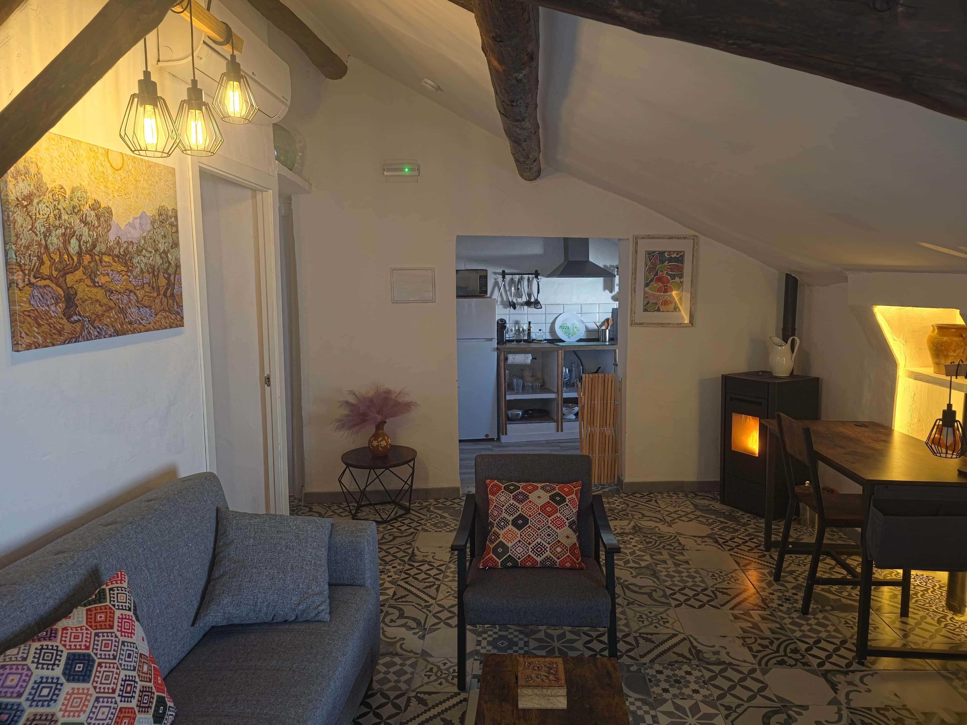 A cozy living room with a sofa, armchair, and coffee table, a kitchen in the background, and a dining area with a table and chairs.