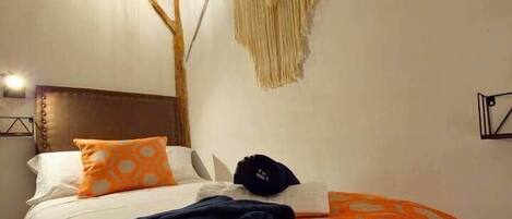 A bed with a patterned blanket, a hanging macrame wall decoration, and a simple headboard.