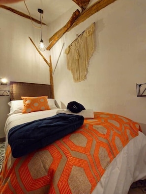Een bed met een bedekt met een patroon, een macramé wanddecoratie en een eenvoudig hoofdbord.