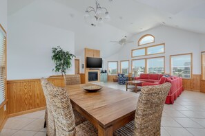 A spacious living area with a wooden dining table, wicker chairs, a red sofa, and a television. - 1428 - Ocean Raves - Pet-Friendly Corolla Escape | Pool & Hot Tub (Corolla)