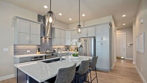 A modern kitchen with a large island, stainless steel appliances, and pendant lighting. - Elegant Home Near TPC Golf Course and Trails (Loveland)
