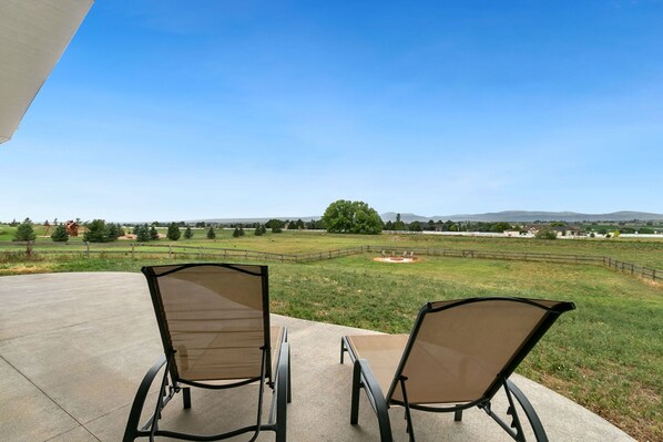 A patio with two chairs facing a grassy field and distant hills. - Luxury Home With Spectacular Rocky Mountain Views (Ault)
