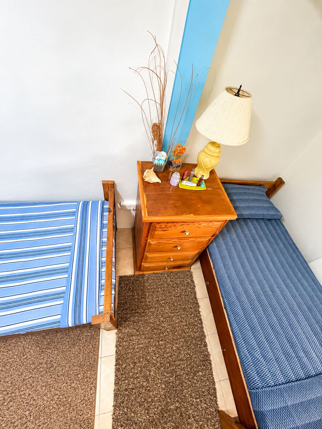 A small, neatly arranged bedroom with two beds, a wooden dresser, and a lamp.