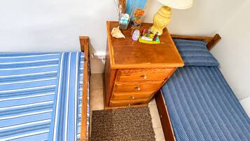 A small, neatly arranged bedroom with two beds, a wooden dresser, and a lamp.
