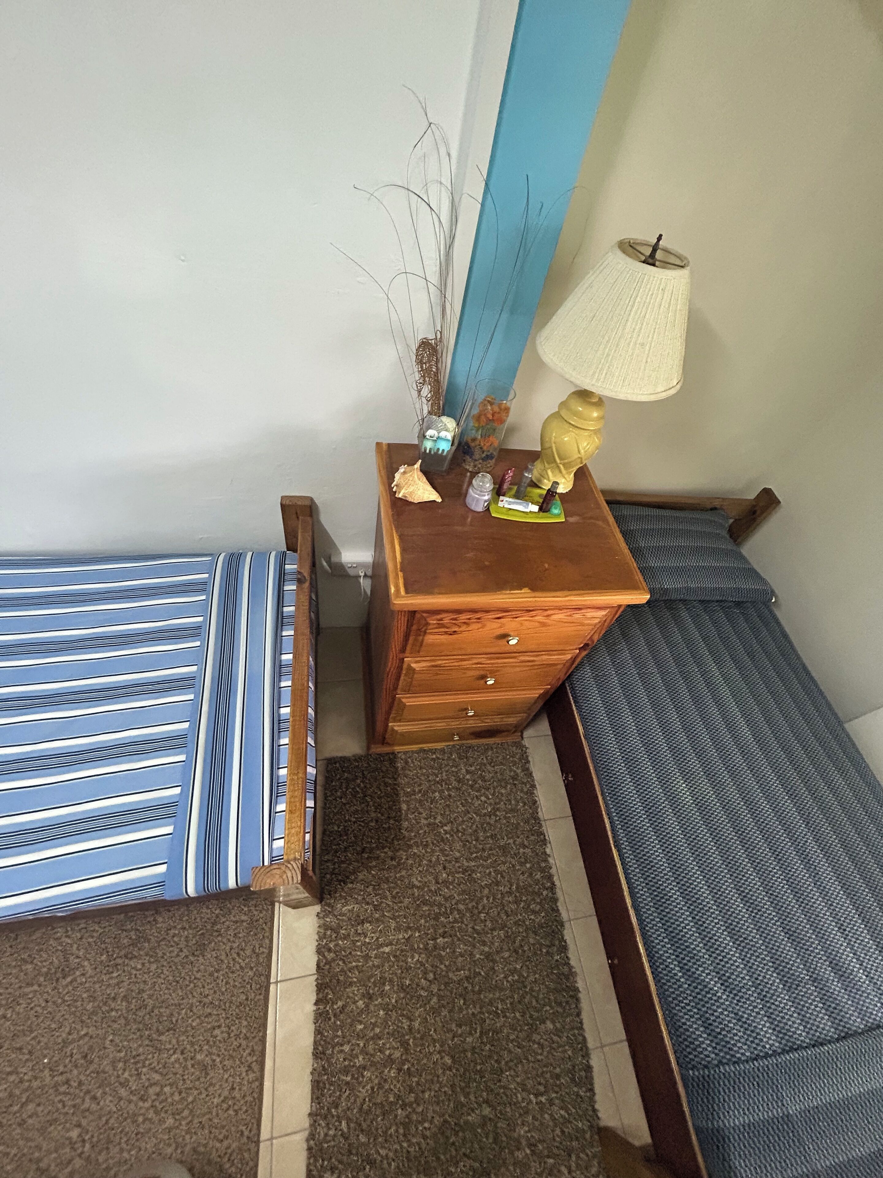 Une petite chambre à coucher, bien rangée, avec un lit simple, une table de chevet, une lampe et une commode.