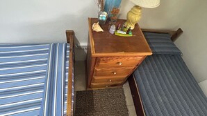 Une petite chambre à coucher, bien rangée, avec un lit simple, une table de chevet, une lampe et une commode.