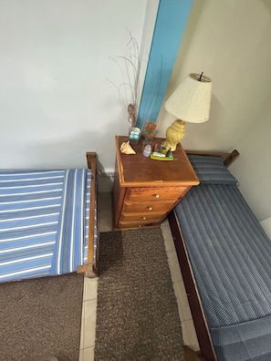 A small, neatly arranged bedroom with a single bed, a nightstand, a lamp, and a dresser. - NIZA’S PLACE—Cozy Mountainside Villa with Ocean view. (Paix Bouche)