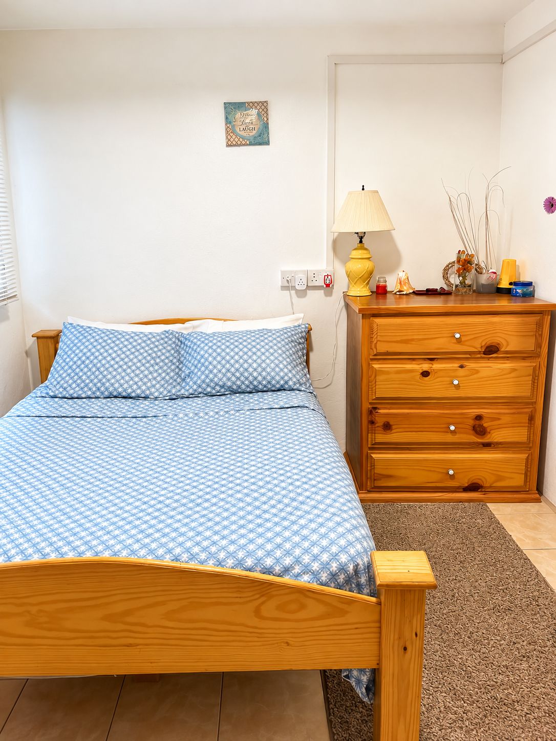 A bedroom with a wooden bed, a nightstand with a lamp, a dresser, and a small wall decoration.