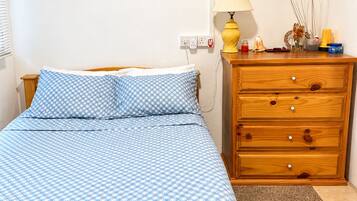 A bedroom with a wooden bed, a nightstand with a lamp, a dresser, and a small wall decoration.