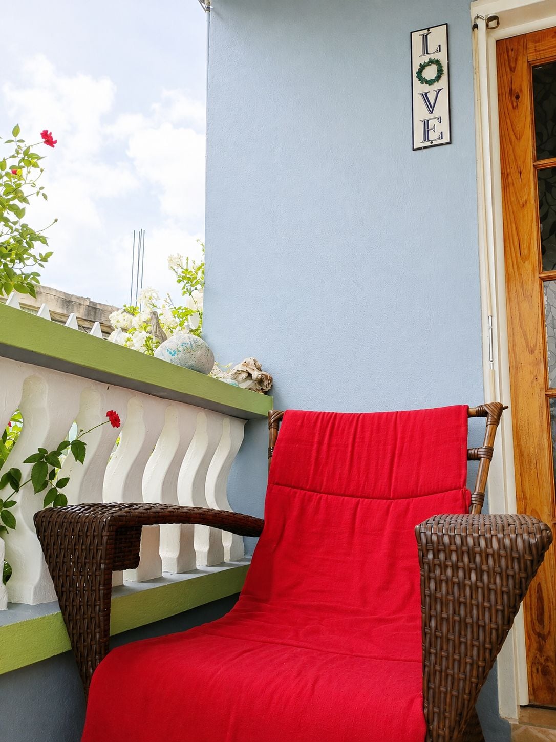 A wicker chair with a red cushion, a white balustrade, and a 'LOVE' sign on a light blue wall.