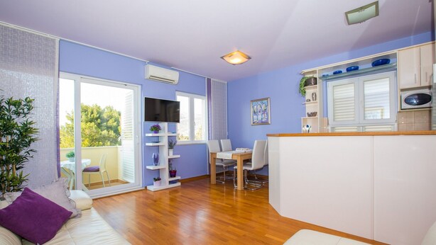 A modern living room with a sofa, a dining table, and a kitchen area with cabinets and a TV. - Apartment 3 beaches with free parking (Dubrovnik)
