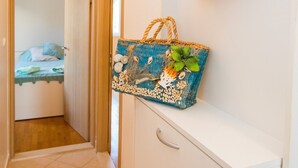 A hallway with a bed in the background, a decorative wall hanging, and a wicker basket on a shelf. - Apartment 3 beaches with free parking (Dubrovnik)