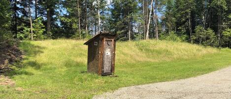 A small wooden structure with a door, surrounded by a grassy area and trees.