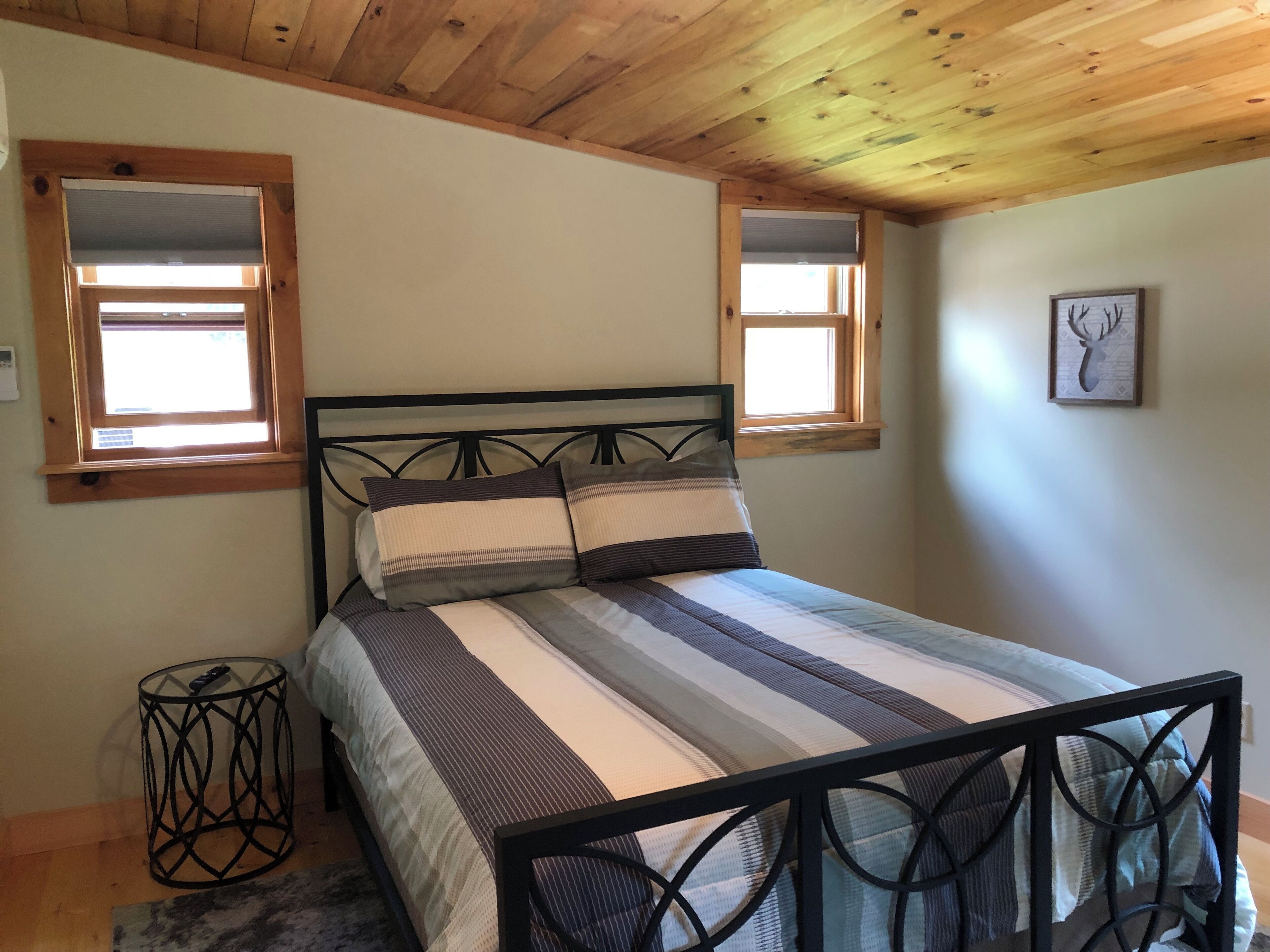 Une chambre à coucher avec un lit, deux fenêtres, un tableau représentant un cerf encadré et une petite table.