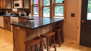 Une cuisine avec des meubles de rangement en bois, un îlot central doté de tabourets, un four à micro-ondes et une cuisinière.