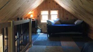 Une chambre mansardée chaleureuse avec un plafond en pente, un lit, un bureau et une fenêtre laissant entrer la lumière naturelle.