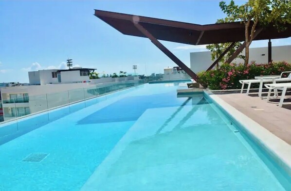 Relax by the rooftop pool surrounded by comfortable lounge chairs and a shaded area.