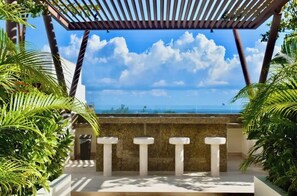 Relax in a serene ocean-view setting surrounded by lush greenery and a wooden pergola.