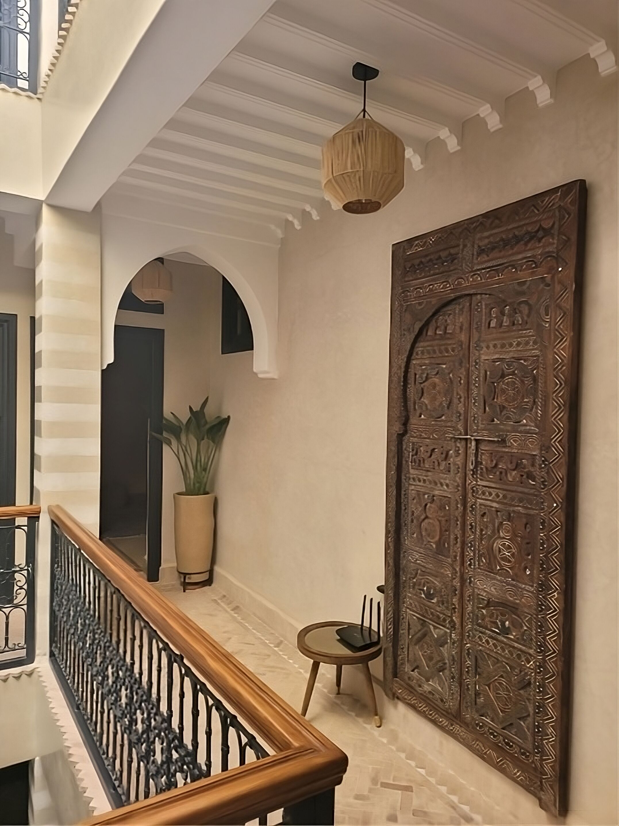 A hallway with a wooden railing, a large ornate door, and a hanging light fixture.