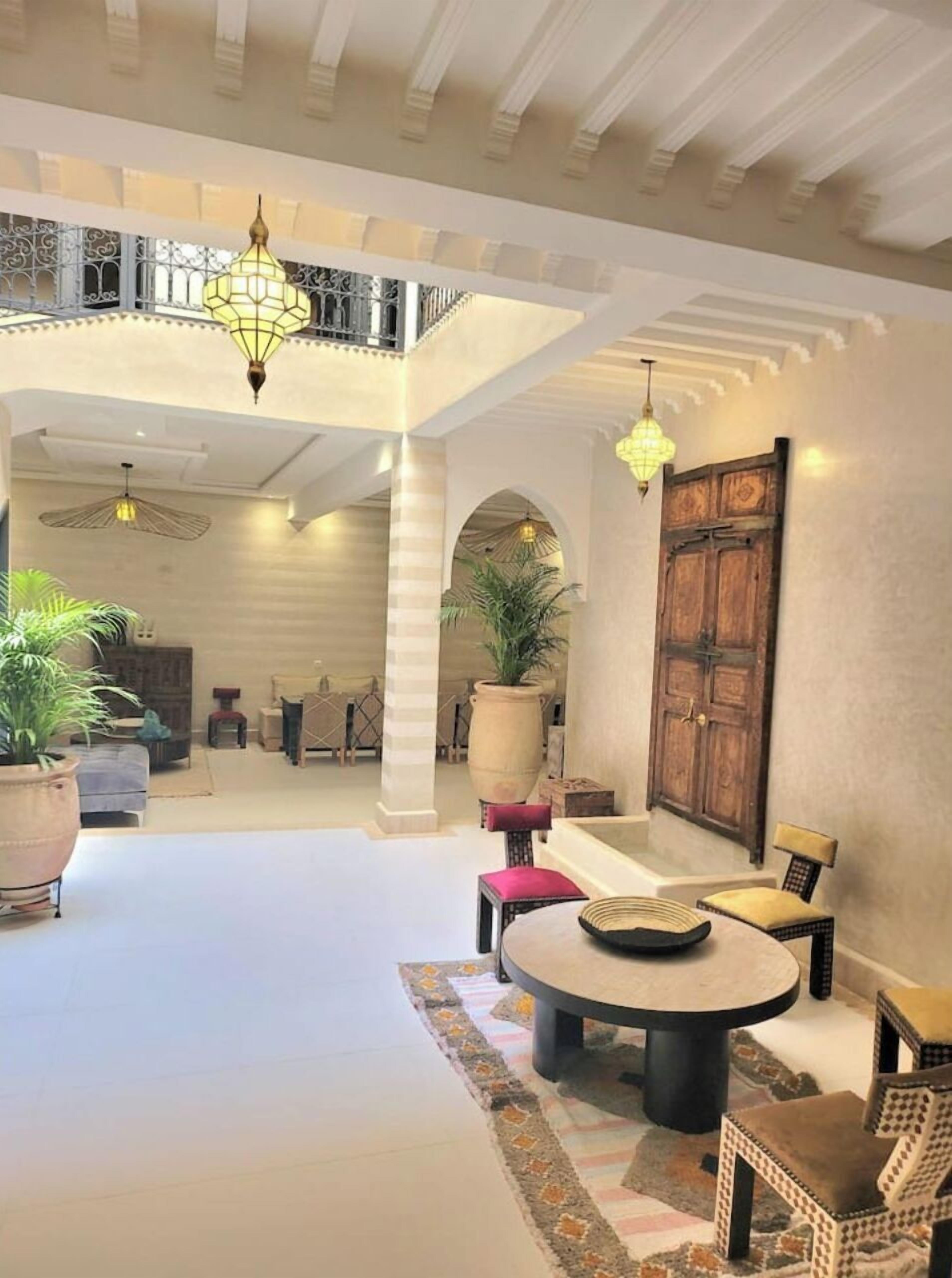 A spacious lobby with a high ceiling, a central seating area with a round table, and multiple hanging lamps.