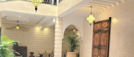 A spacious lobby with a high ceiling, a central seating area with a round table, and multiple hanging lamps.