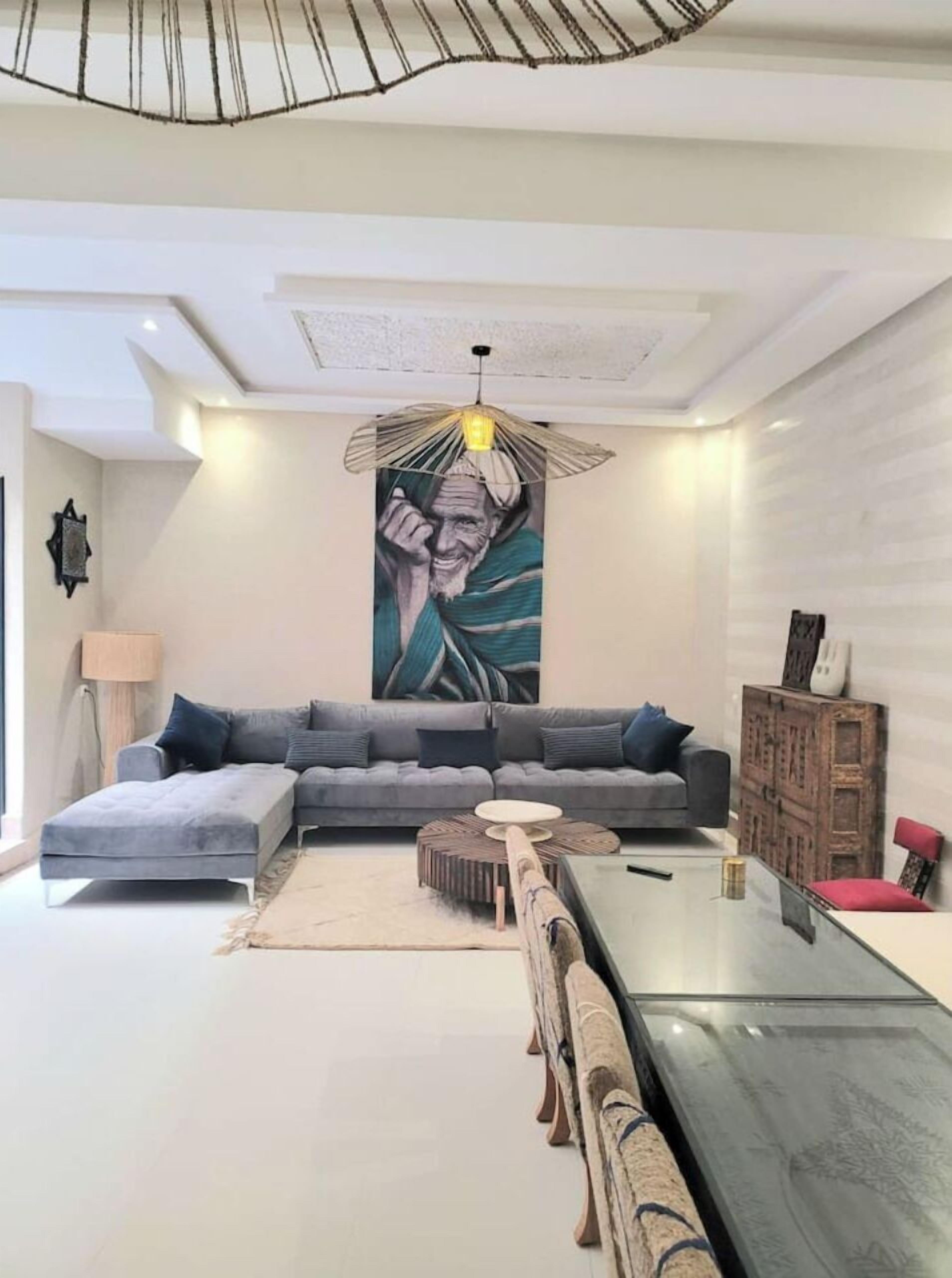 Uma sala de estar moderna com um sofá modular cinza, uma mesa de centro de vidro e uma luminária pendente singular.