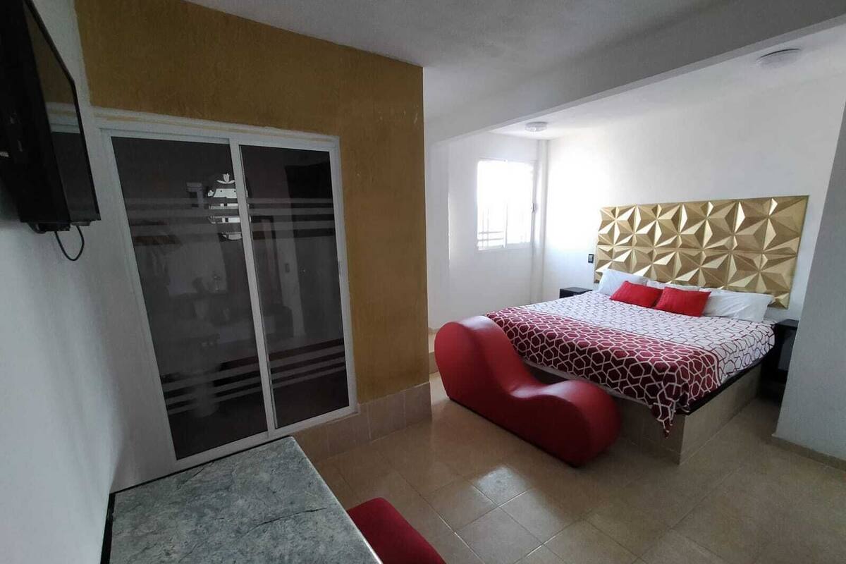 A bedroom with a bed, a red chair, a small table, and a sliding door.