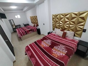 Ein Hotelzimmer mit zwei Betten, jedes mit einer rot-weißen Musterdecke, einem goldenen geometrischen Kopfteil und einem kleinen Nachttisch mit einer Lampe.