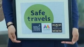 A person holding a framed certificate with the text "Safe travels" and logos of the World Travel & Tourism Council, Edomex, and Hotel Encanto.
