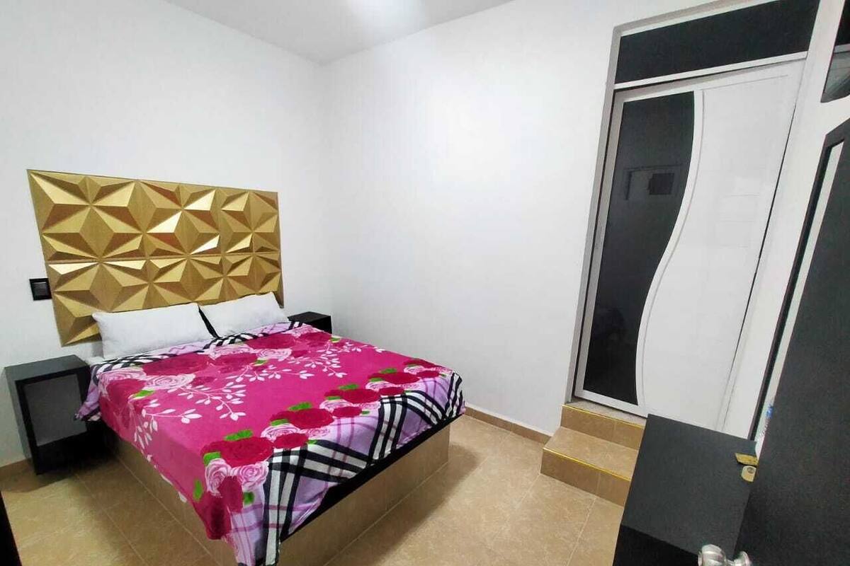 A bedroom with a bed, a nightstand, a headboard, and a door.
