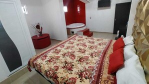 A bedroom with a large bed, a red accent wall, and a small red table with a vase.