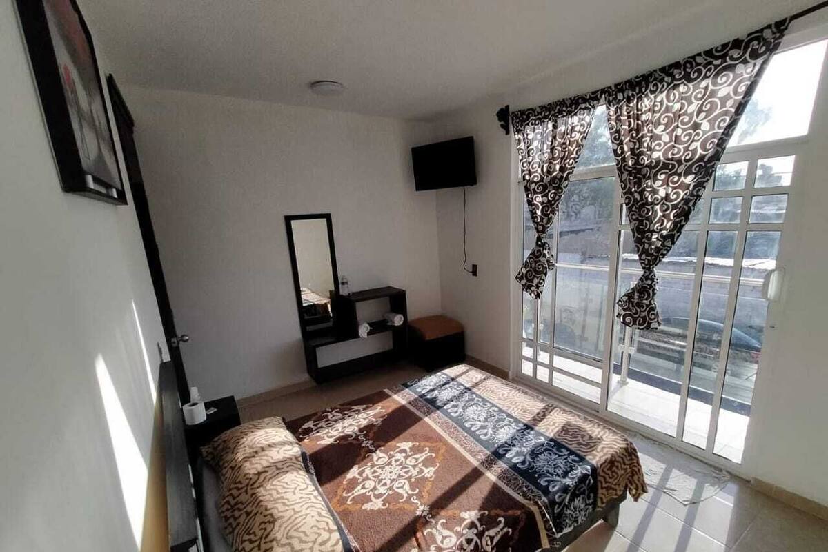 A bedroom with a bed, a TV, a window with curtains, and a small table.