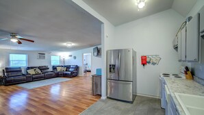 Ein geräumiges Wohnzimmer mit einem großen Ecksofa, einem Deckenventilator und einer Küchenzeile, ausgestattet mit einem Edelstahlkühlschrank und einem weißen Herd.
