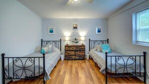Ein Schlafzimmer mit zwei Einzelbetten, einem Nachttisch, einem Deckenventilator und einem Fenster mit Jalousien.