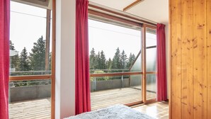 A bedroom with a large window, a wooden floor, and a bed with a white blanket. - Appartement 6 pers proche pistes (Chamrousse)