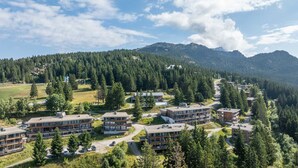 A resort with multiple buildings surrounded by dense forest and mountains. - Appartement 6 pers proche pistes (Chamrousse)