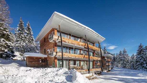 A multi-story wooden chalet with balconies, surrounded by snow-covered trees. - Appartement 6 pers proche pistes (Chamrousse)