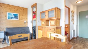 Ein gemütliches Zimmer mit einem Holztisch, zwei Stühlen, einem grauen Sofa und einer Holzkabine mit Glastüren.