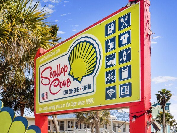A colorful billboard for Scallop Cove, featuring a Shell logo, various amenities icons, and a website URL. - Cape San Blas w/3BR, Pet Friendly & Sunset Views (Port St. Joe)