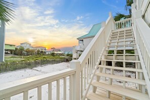 A coastal property with a wooden staircase leading to a balcony, overlooking a sandy beach and residential buildings. - Cape San Blas w/3BR, Pet Friendly & Sunset Views (Port St. Joe)
