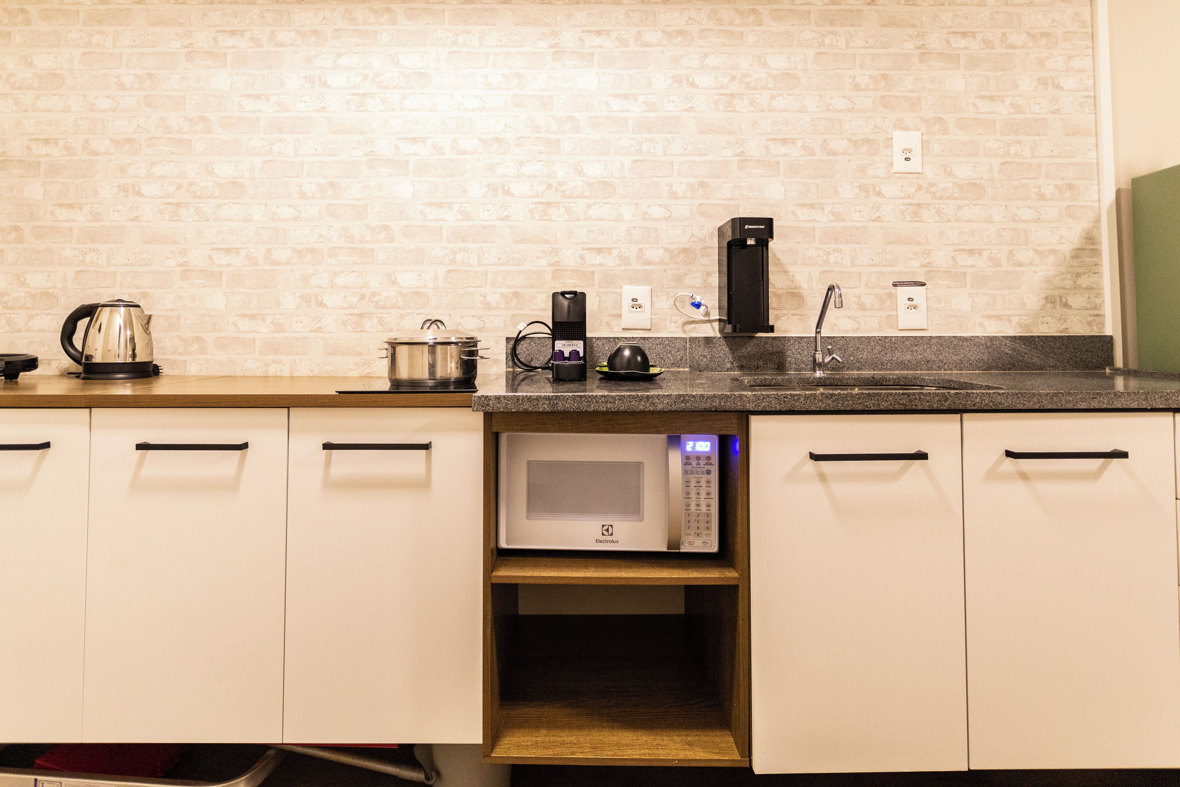 Une cuisine équipée d’un four à micro-ondes, d’une bouilloire et d’une machine à café, le tout posé sur le plan de travail.