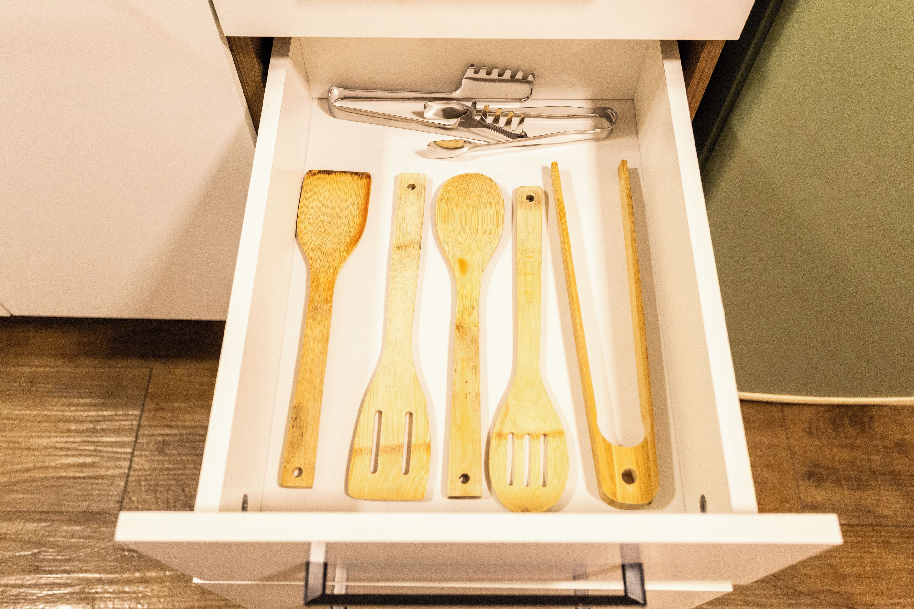 A drawer containing wooden kitchen utensils including a spatula, spoon, and tongs.