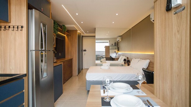 A compact hotel room with a kitchenette, a bed with a view, and a dining area set for two. - Studio Lume 163 A (São Paulo)