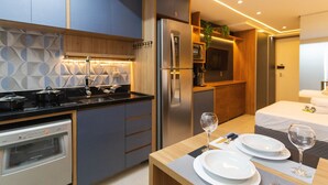 A modern kitchen with a built-in oven, a refrigerator, and a microwave. There is a dining area with a table set for two, including plates, glasses, and cutlery. - Studio Lume 163 A (São Paulo)