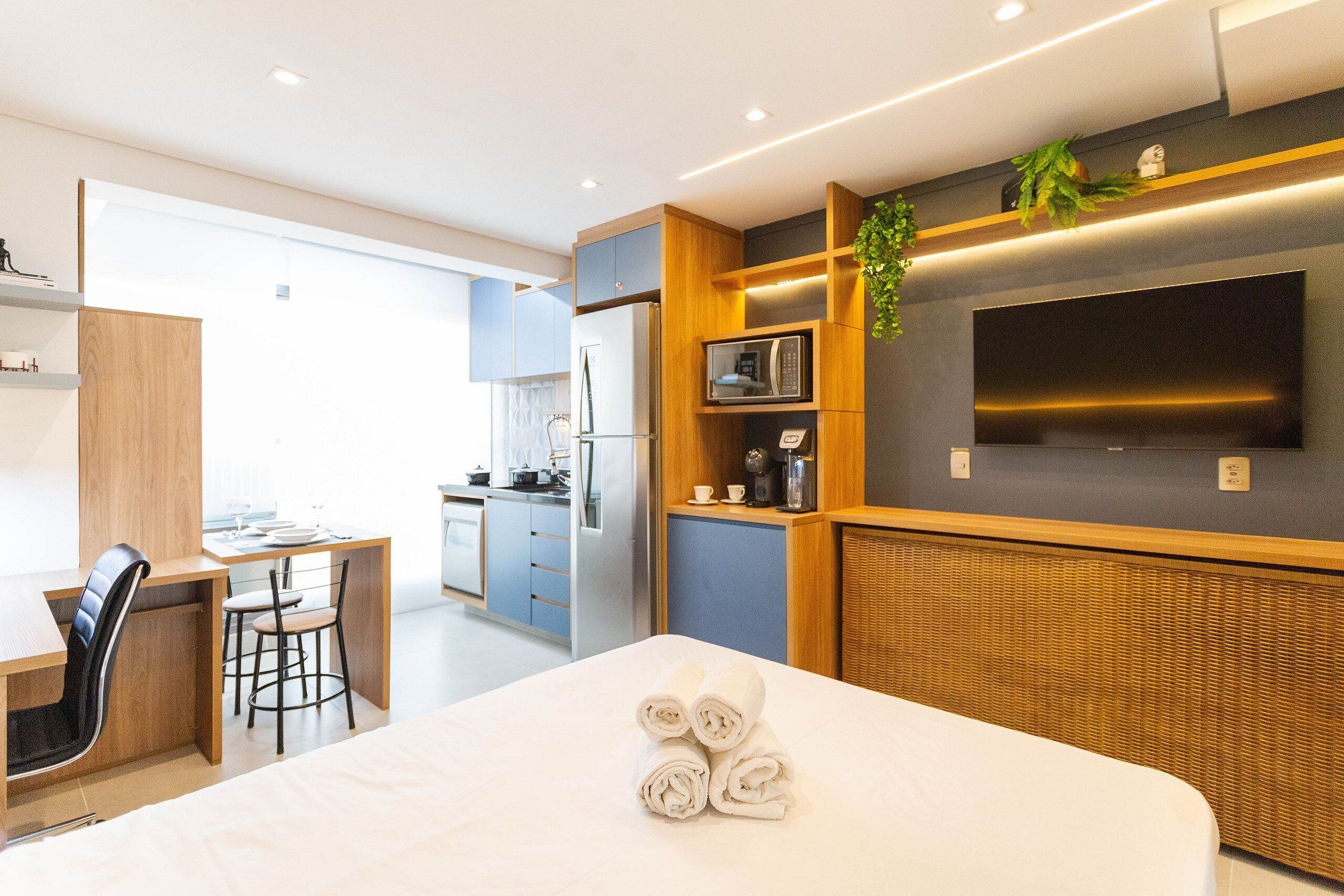 A modern hotel room with a bed, a desk, a chair, a microwave, and a television.