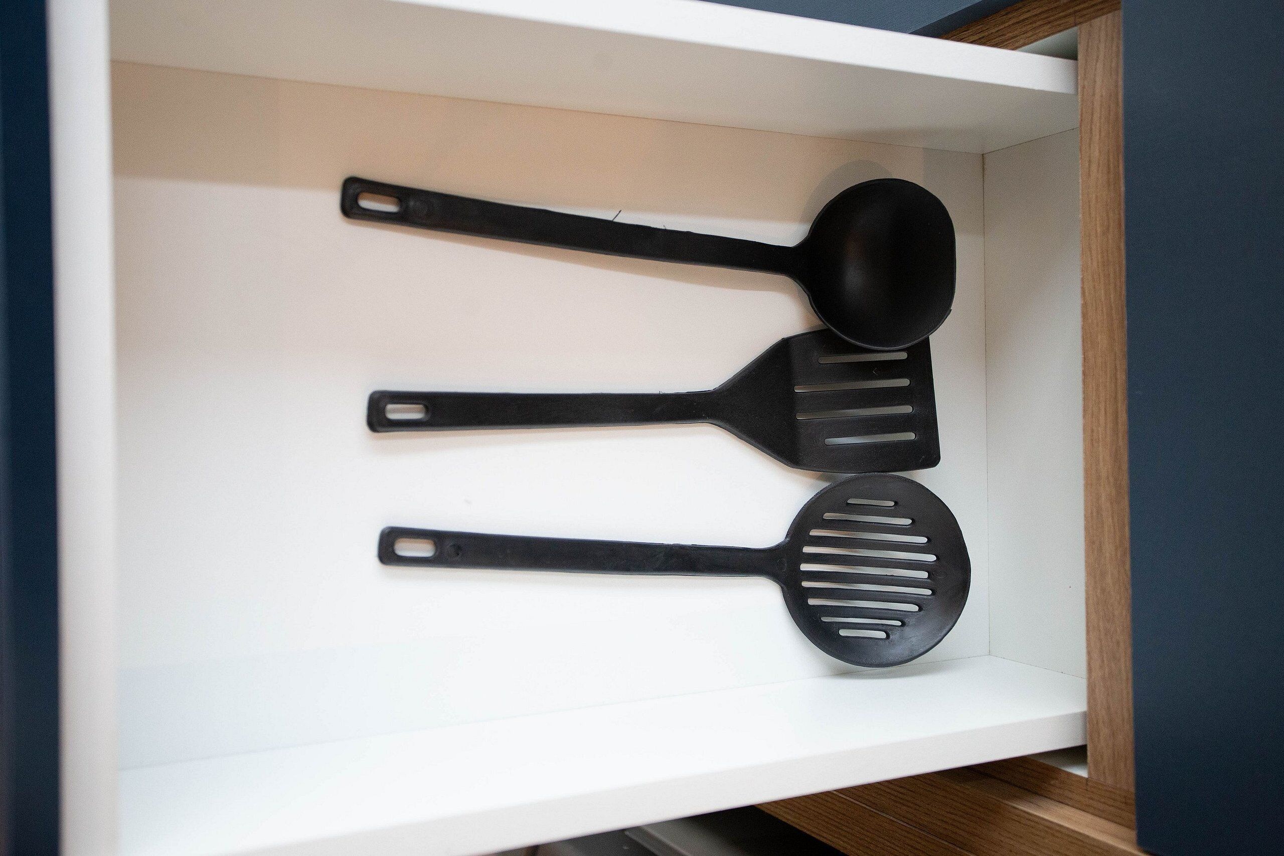 A drawer containing three black kitchen utensils: a slotted spatula, a ladle, and a spatula with a long handle.