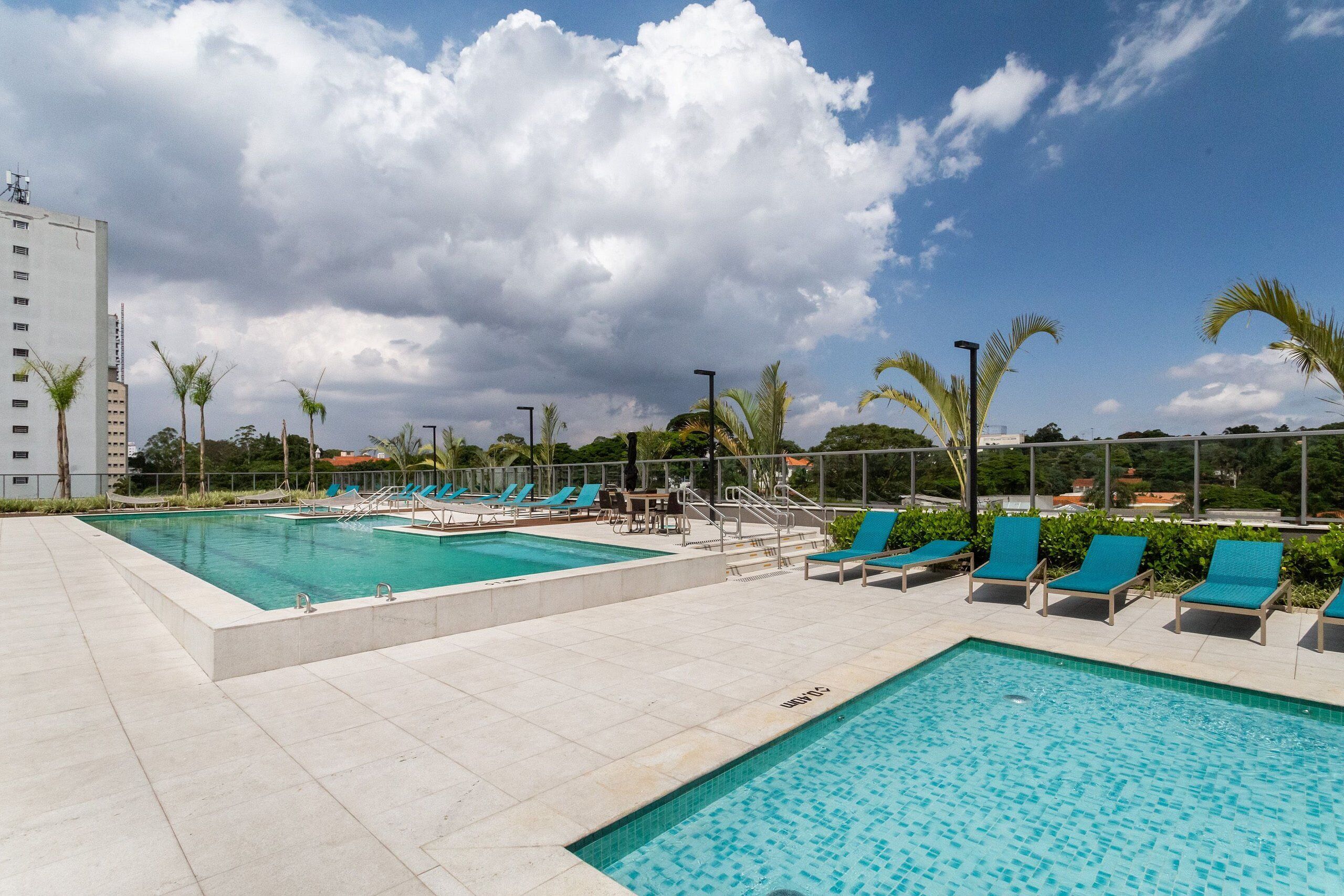 Uma área de piscina com duas piscinas, espreguiçadeiras e palmeiras.
